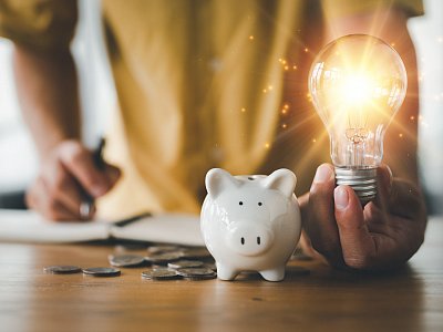 saving energy and money concept. idea for save or investment. businessman holding lightbulb beside piggy bank and coins stacking on desk with note book. - Looker_Studio - stock.adobe.com